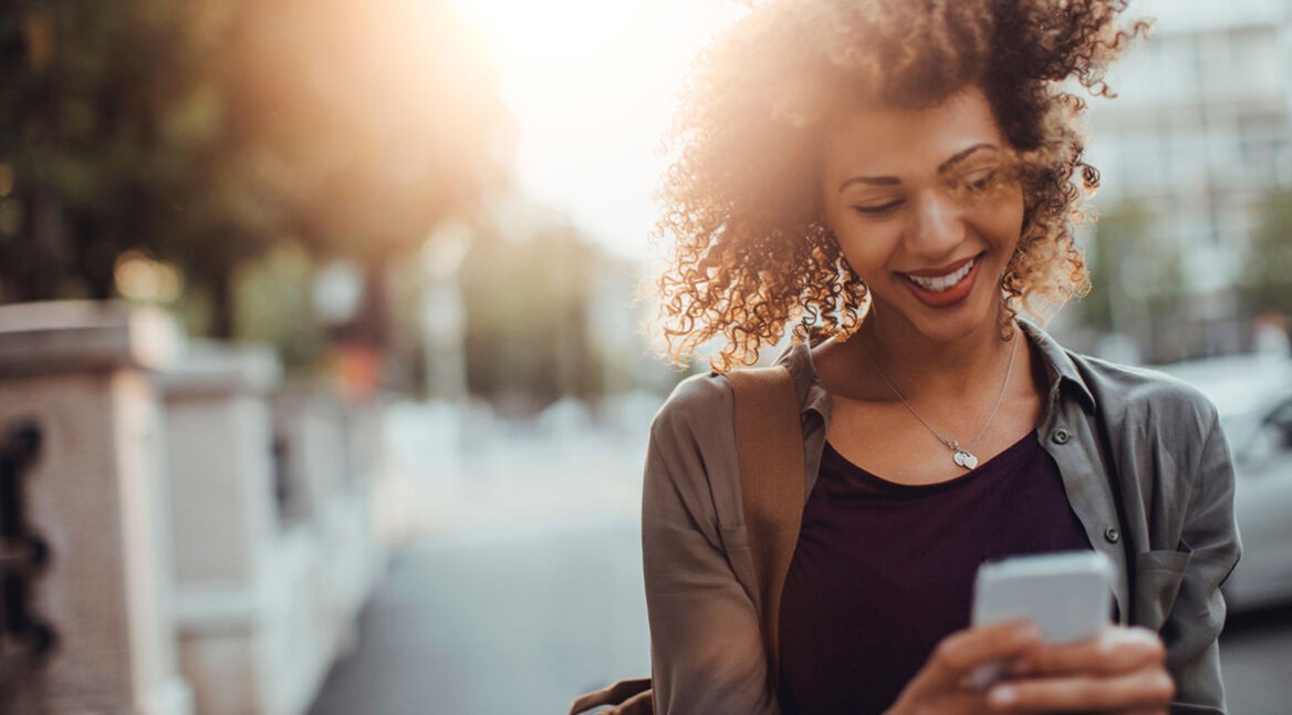 Frau mit lockigen Haaren und Smartphone in der Hand nutzt Highspeed-Internet ohne Limit dank DataPush von Vodafone