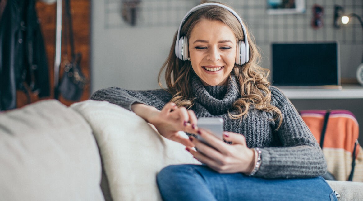Junge Frau auf Sofa hört Podcast
