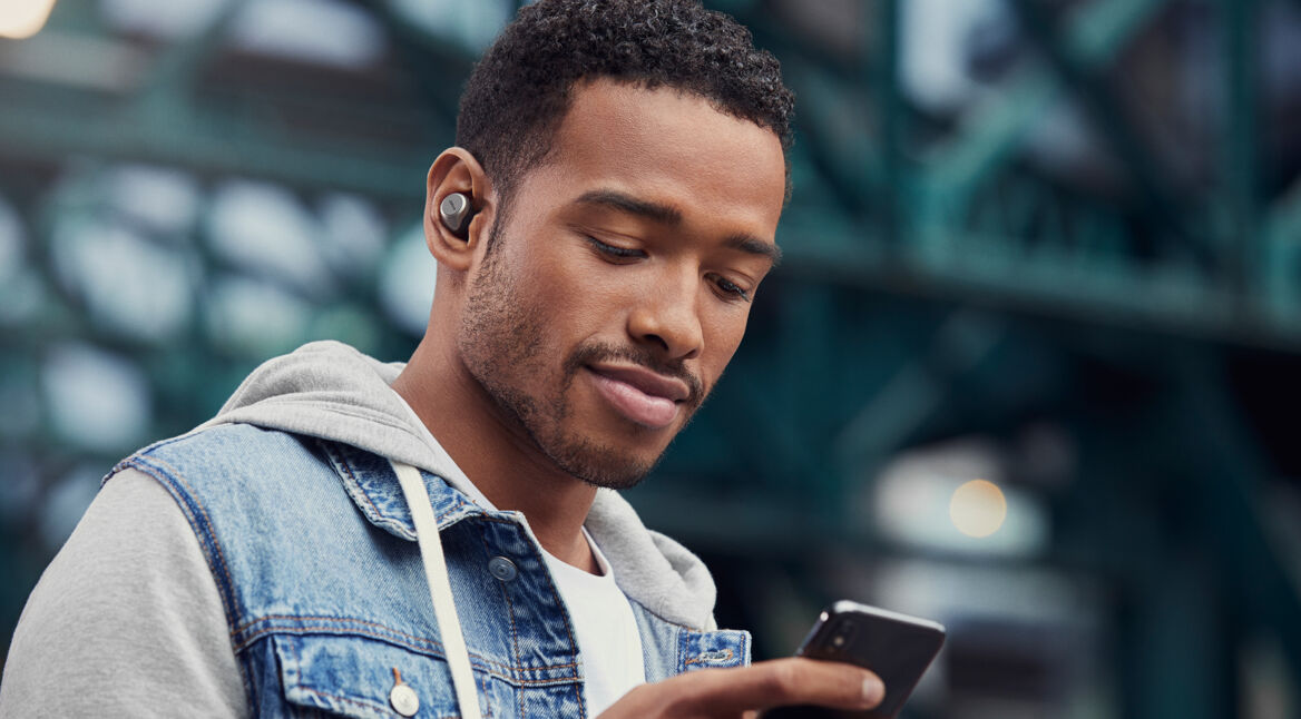 Junger Mann mit Jabra Elite 75t und Smartphone