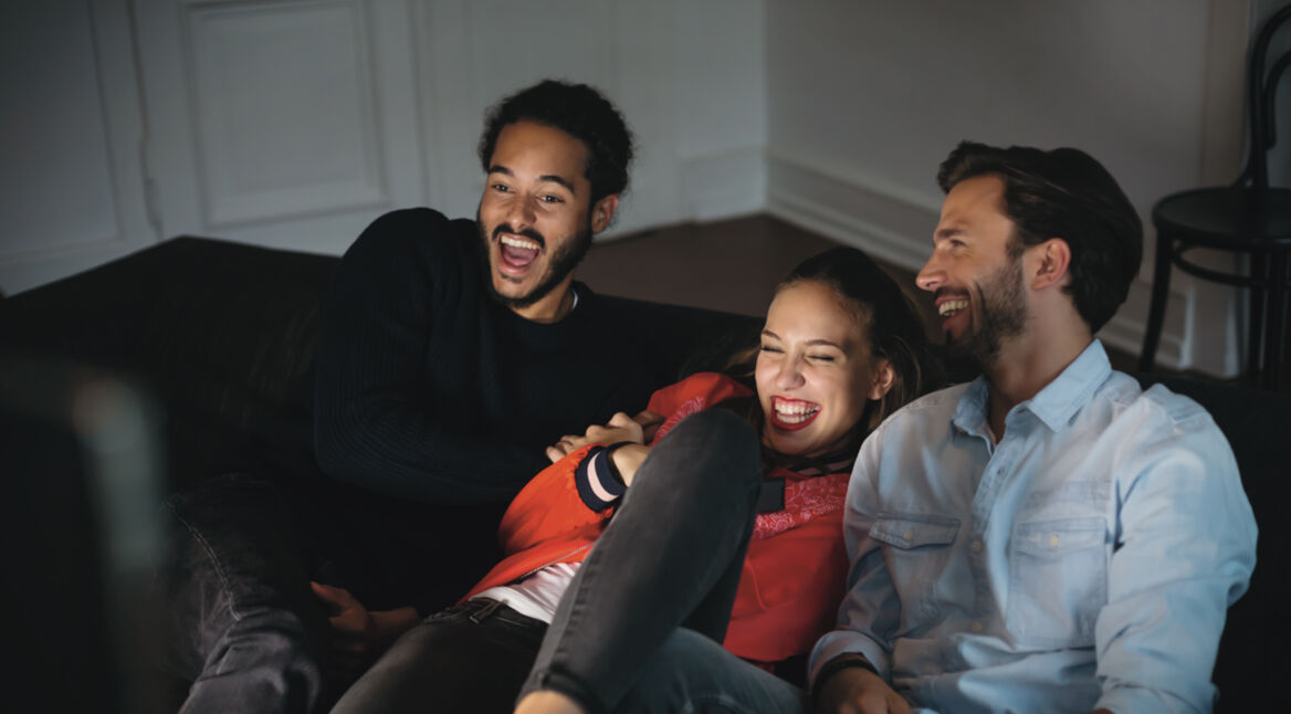 Drei Junge Leute auf dem Sofa freuen sich über die GigaTV-Cable-Senderübersicht