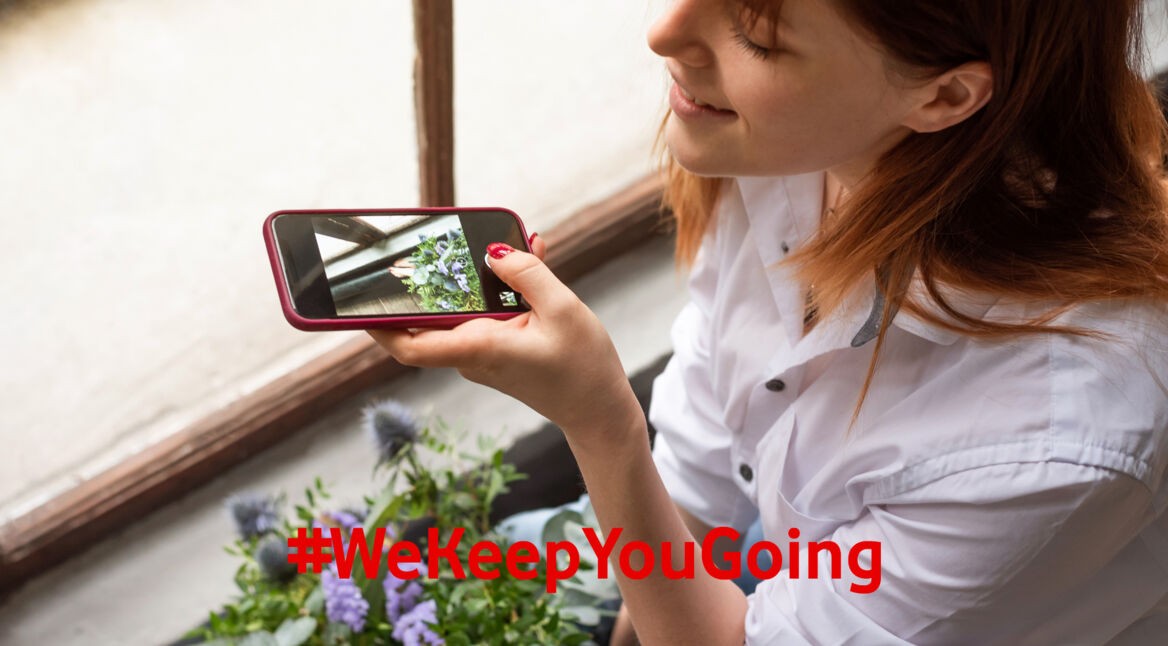 Eine Frau fotografiert einen Blumenstrauß zuhause mit ihrem Smartphone.