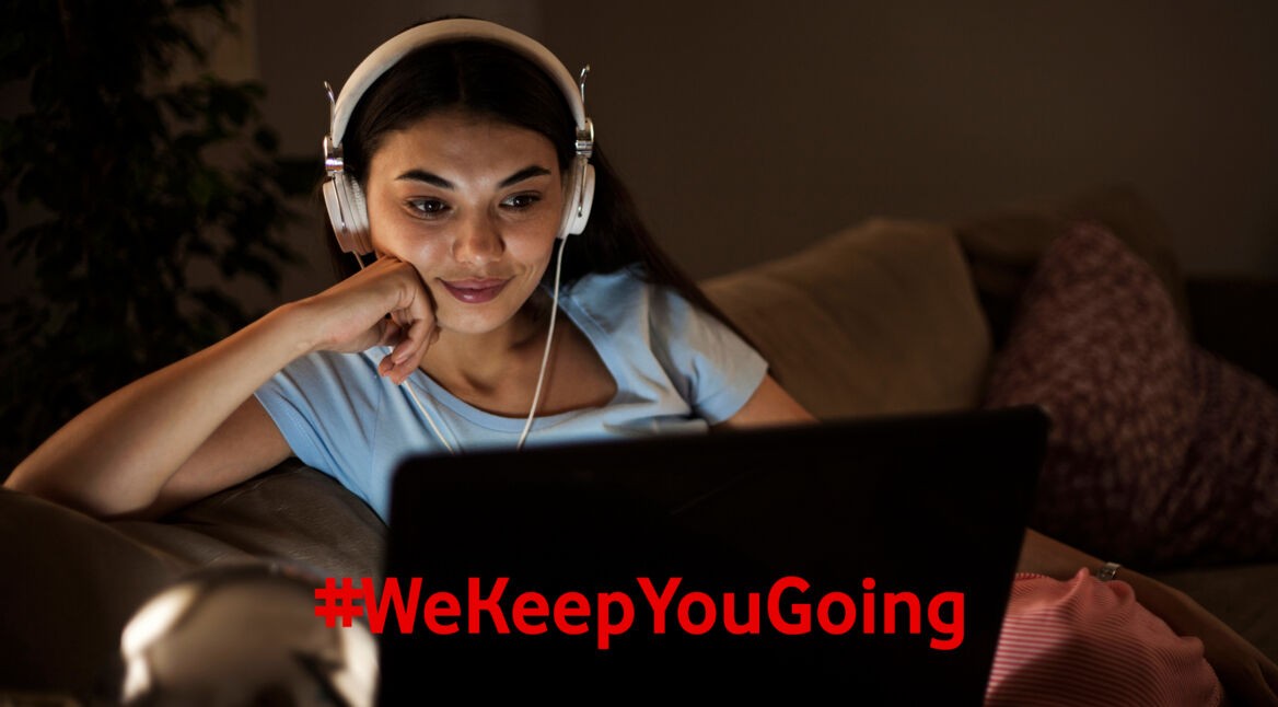 Eine Frau schaut über ihren Laptop und Kopfhörern TV.