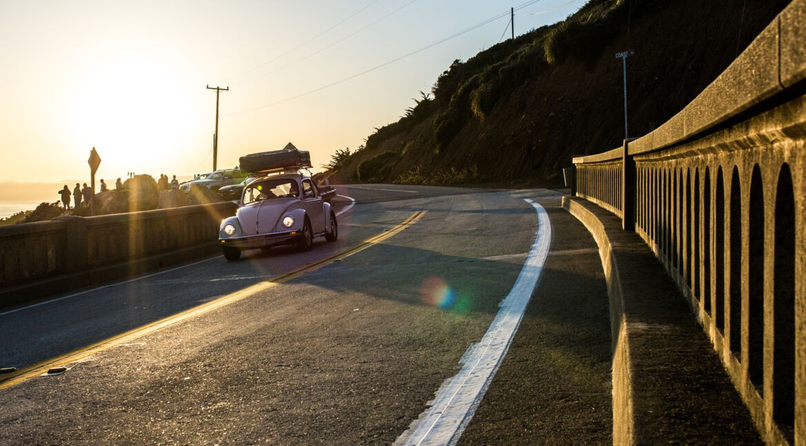 In Reise-Dokus fährt ein weißes Auto im Abendlicht auf einer Straße