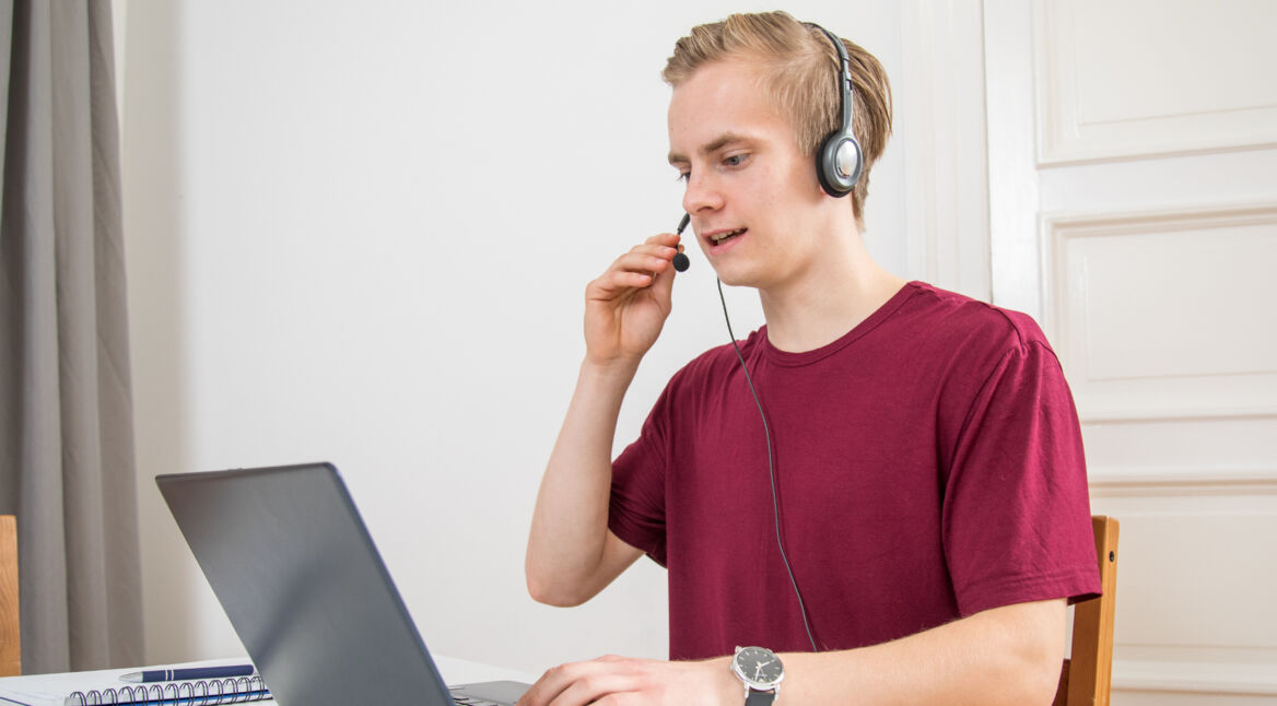 Junger Mann sitzt mit Headset auf dem Kopf vor Laptop