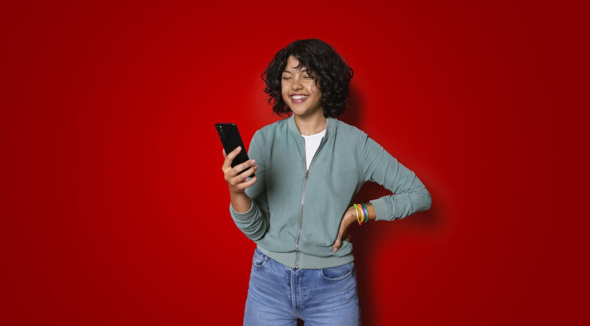 Eine junge Frau schaut lächelnd auf ihr Smartphone während sie die MeinVodafone-App nutzt