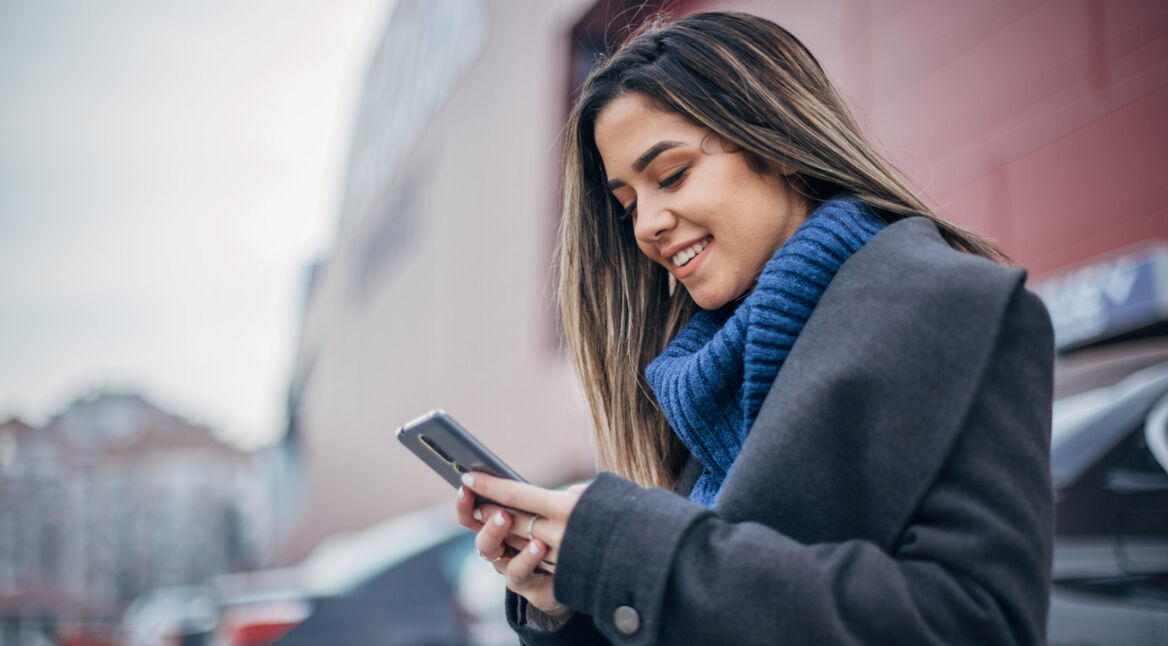 Frau sucht mit dem Smartphone auf einem Parkplatz ihr Auto