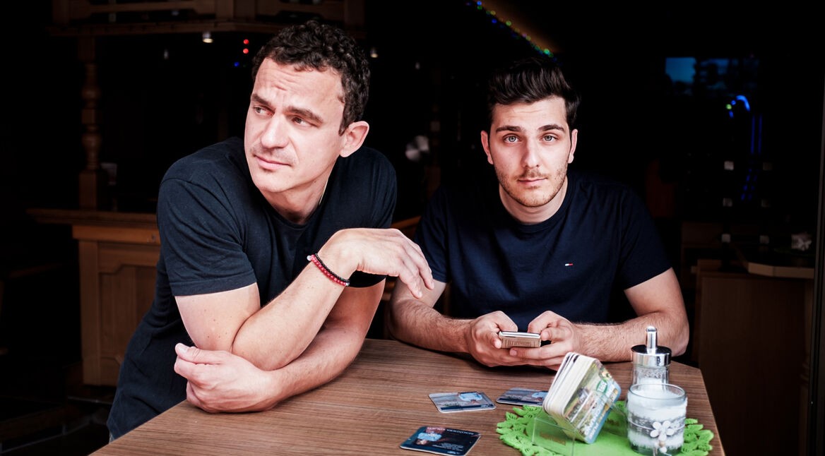 Die Comedy-Autoren Christian Huber und Tarkan Bagci stehen an einem Tisch in einer Kneipe