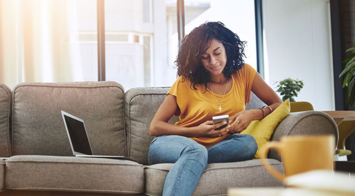 Frau sitzt auf Couch und nutzt ihr Handy.