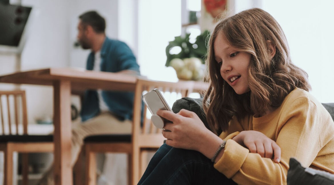 Mädchen mit Smartphone, im Hintergrund der Vater