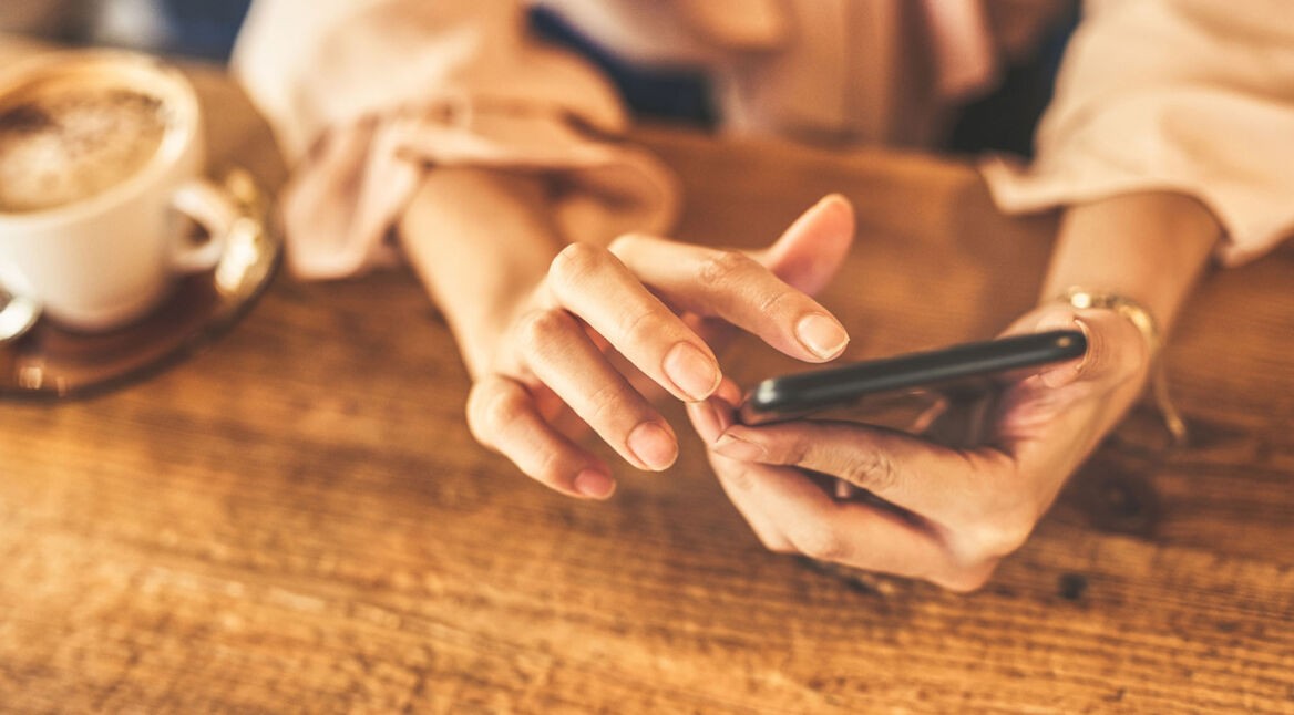 Frau sitzt im Café und bedient ihr Smartphone