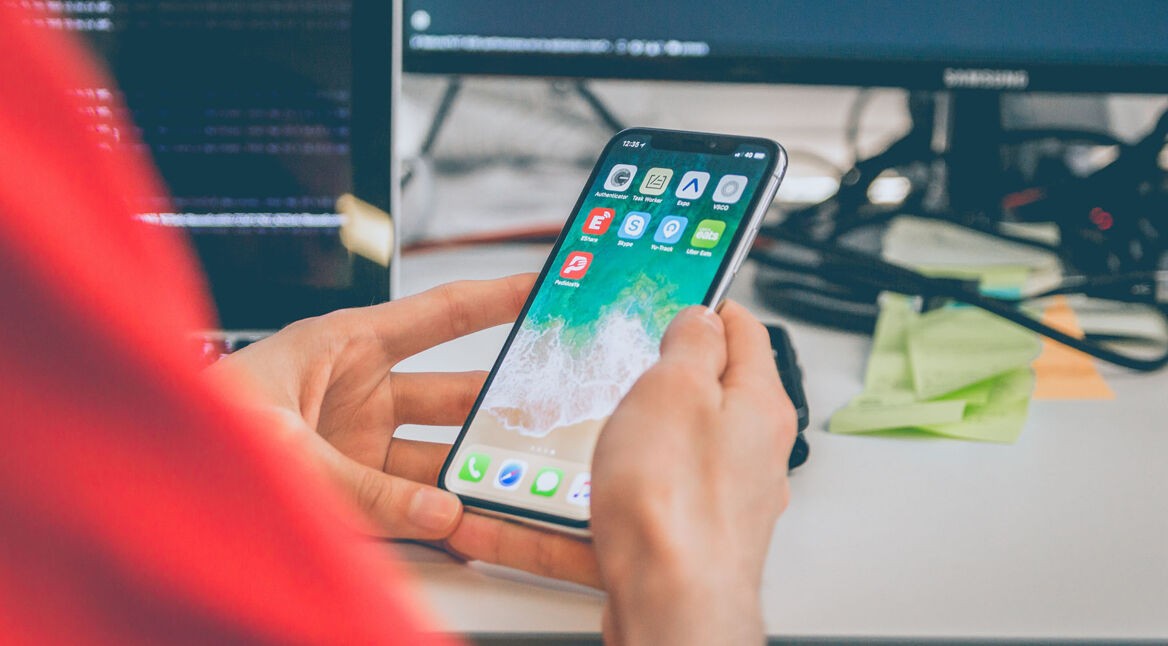 Mann am Schreibtisch, hält iPhone in der Hand