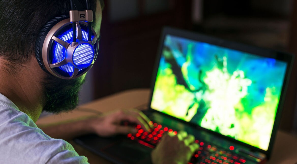 Ein Mann spielt mit Headset auf seinem Laptop ein Spiel.