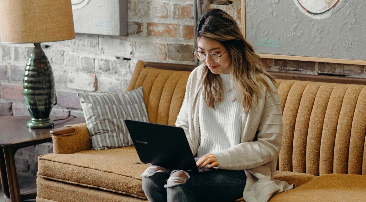 Frau sitzt mit Laptop auf dem Sofa im Wohnzimmer