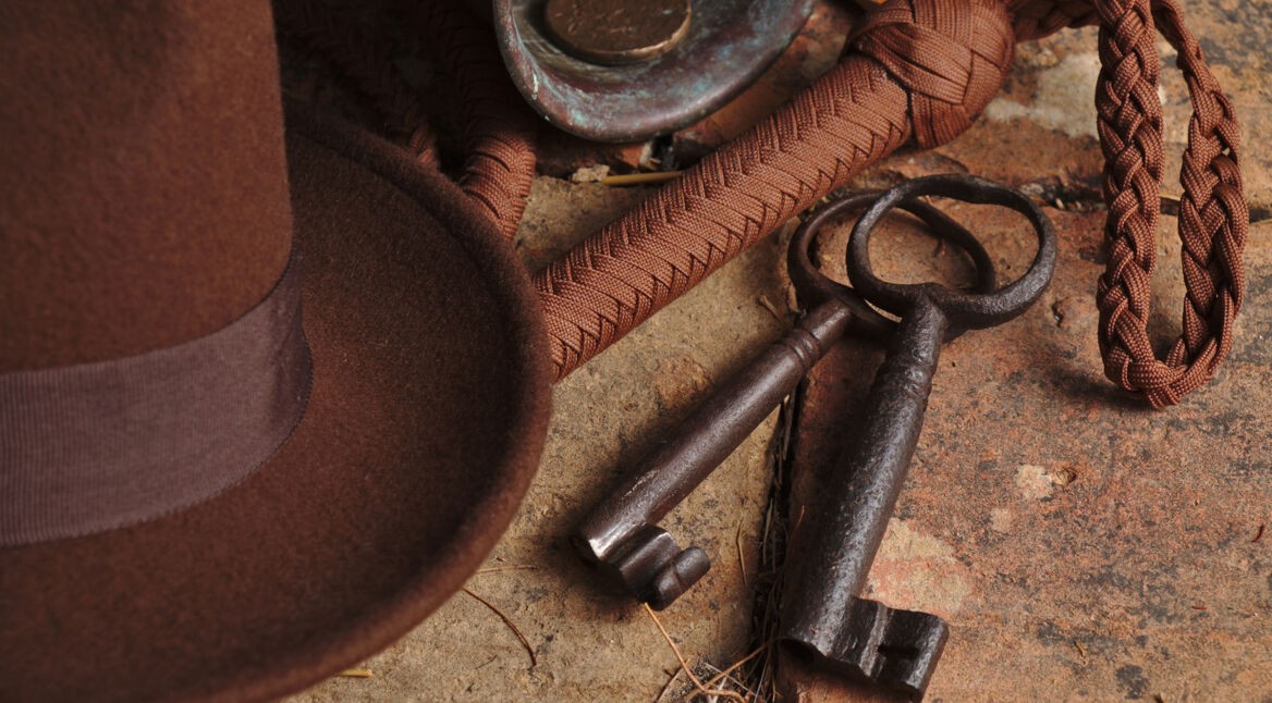 Ein Hut, ein Schlüsselbund und ein Seil liegen auf einem erdigen Boden.