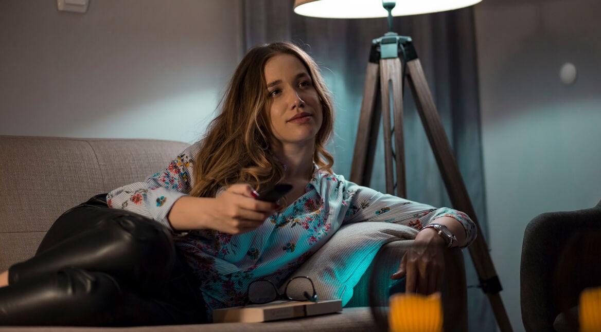 Frau sitzt mit Fernbedienung auf der Couch