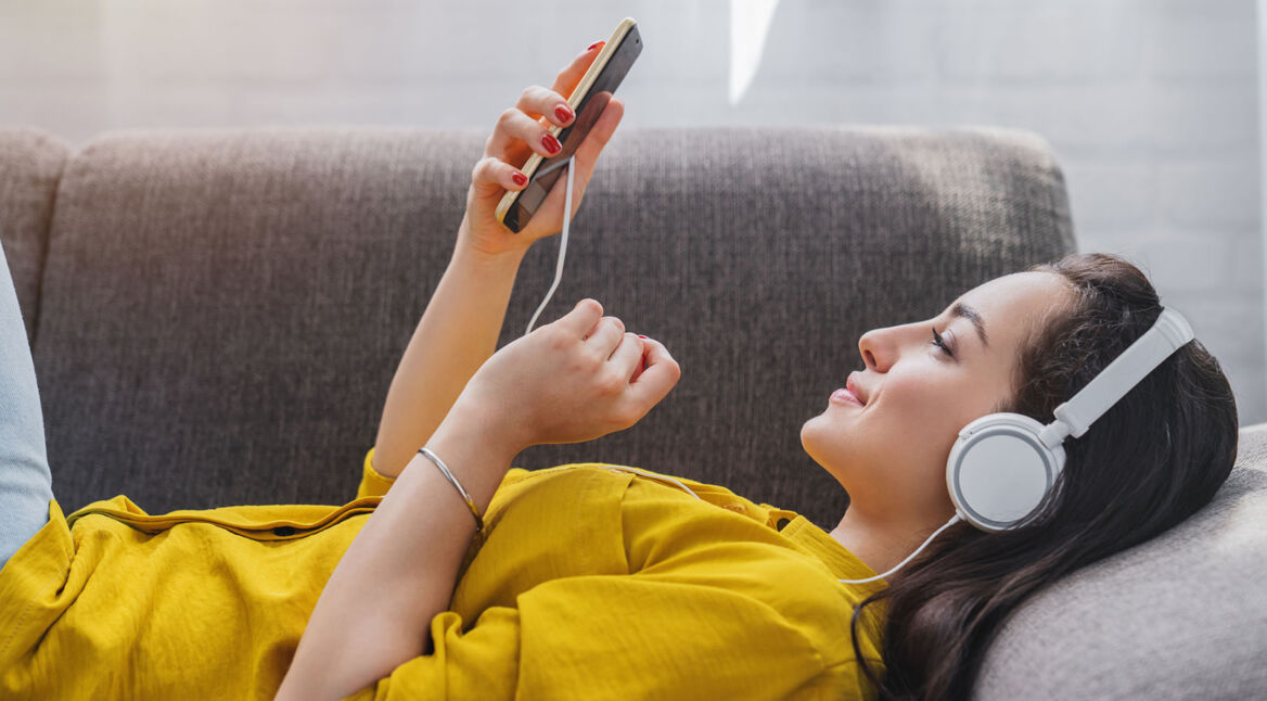 Frau liegt auf dem Sofa und hört mit dem Smartphone Musik
