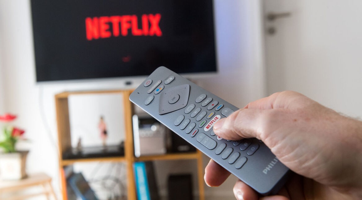 Fernbedienung mit Netflix-Button vor Fernseher, auf dem Netflix startet