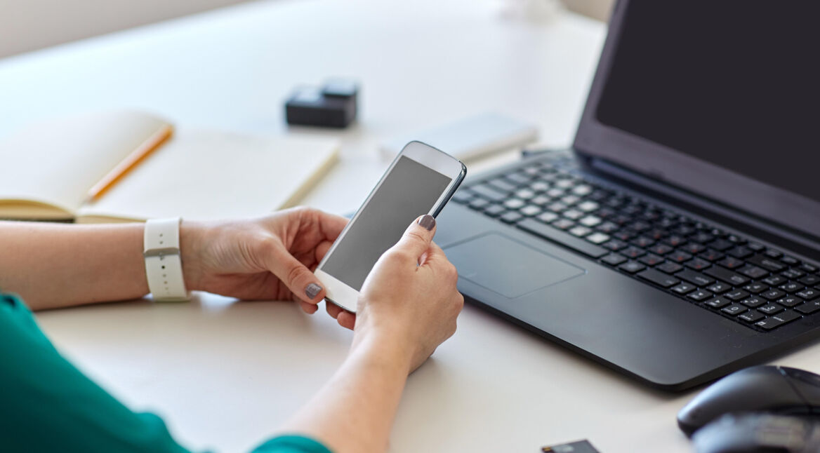 Hände halten Android-Handy vor Laptop