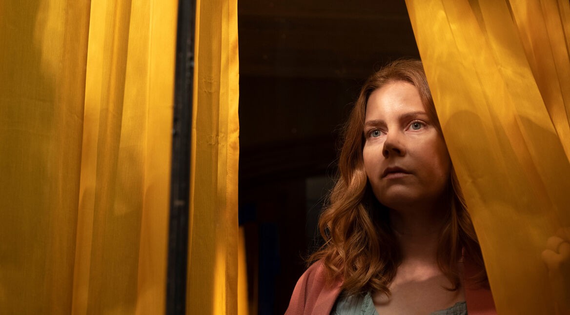 Anna Fox (Amy Adams) sieht aus einem Fenster mit gelben Vorhängen im Film "The Woman in the Window".