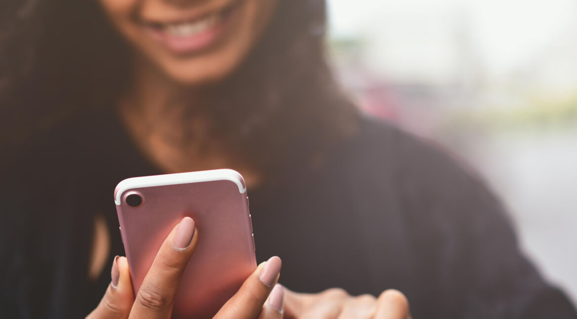 Lachende Frau hält iPhone in Rosegold – iOs 15 Rückblicke