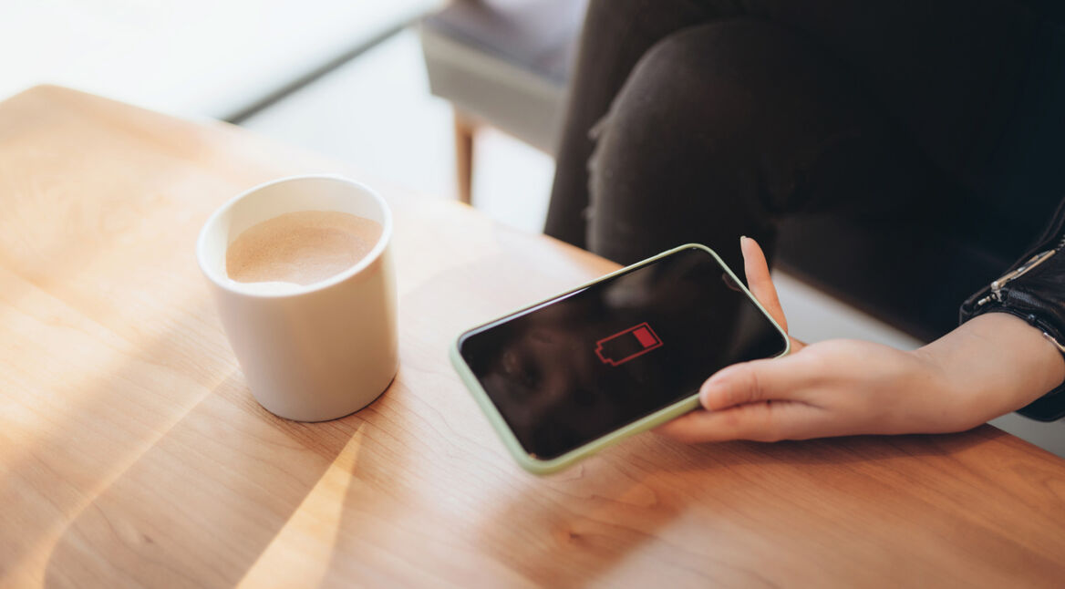 Frau im Café hält Handy mit leerem Akku