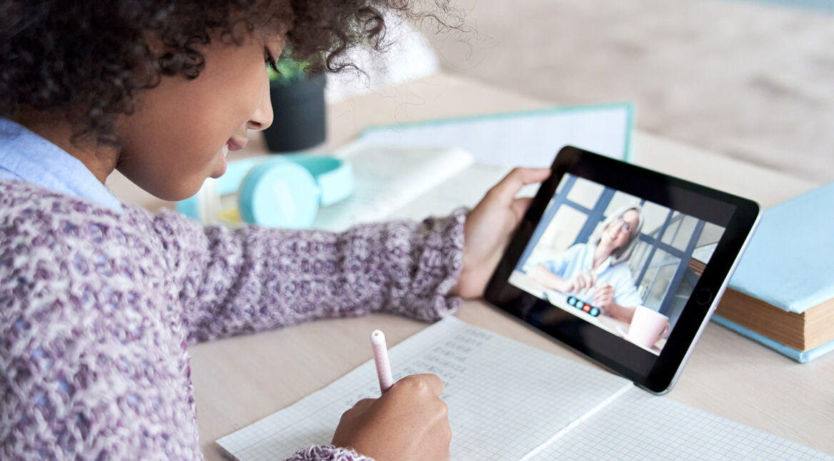 Ein Mädchen bearbeitet Schulaufgaben mithilfe einer Betreuerin über das Tablet.