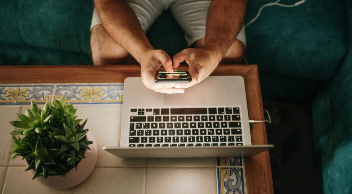 Mann sitzt mit Smartphone am Laptop