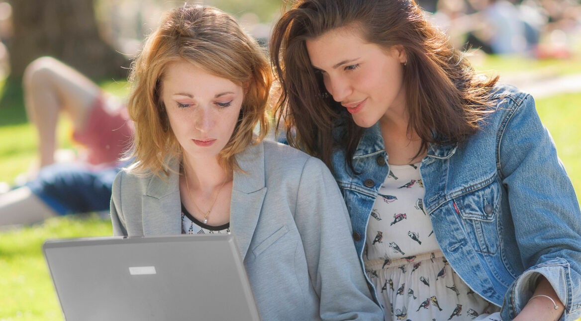 Zwei Frauen im Park gucken auf einen Laptop-Bildschirm