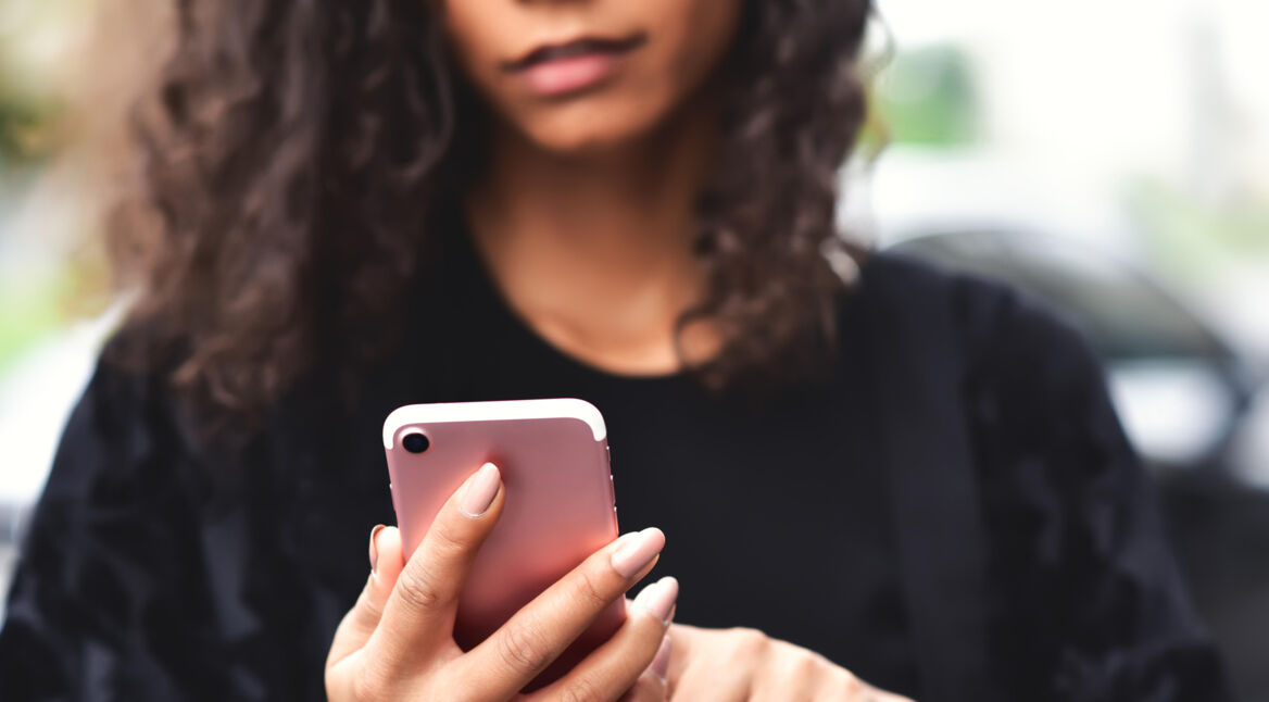 Frau mit Locken guckt auf ihr iPhone SE