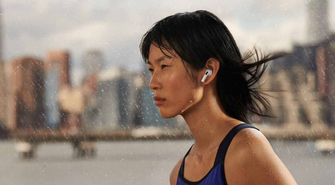 Sportliche Frau trägt AirPods 3 im Freien umgeben von Tropfen