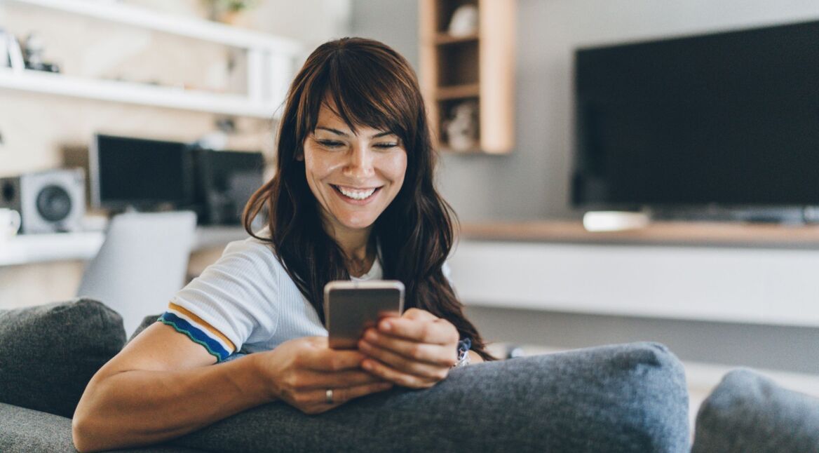Frau schaut lächelnd auf ihr Handy.