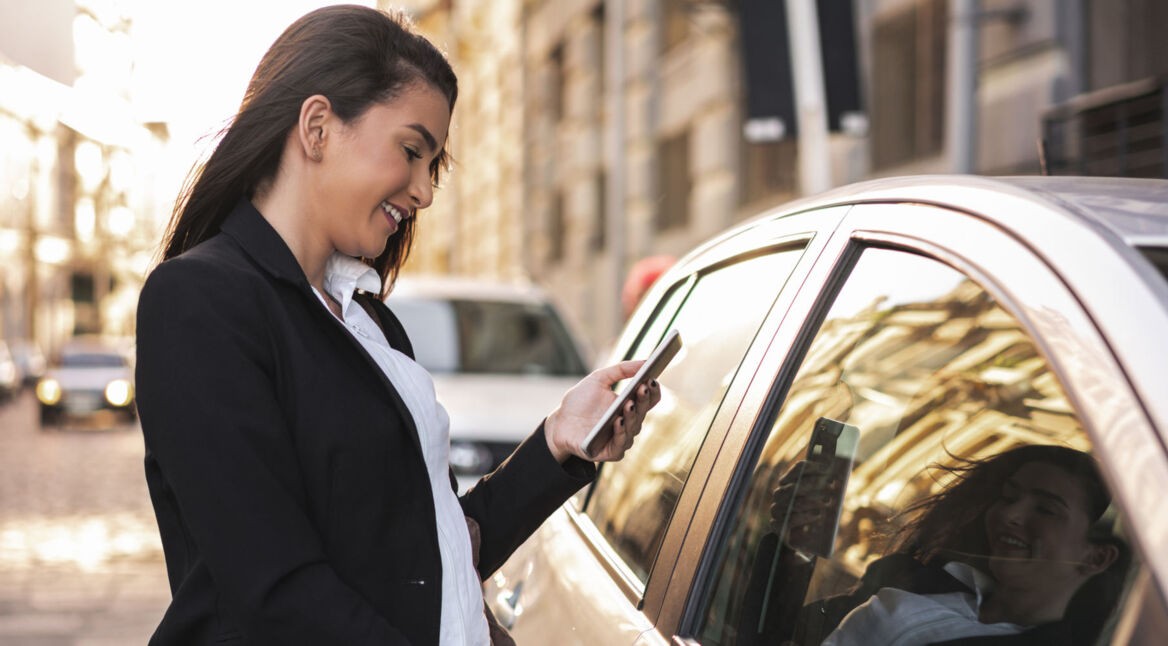 Frau öffnet Tür eines Autos, während sie ihr Smartphone in der Hand hält.
