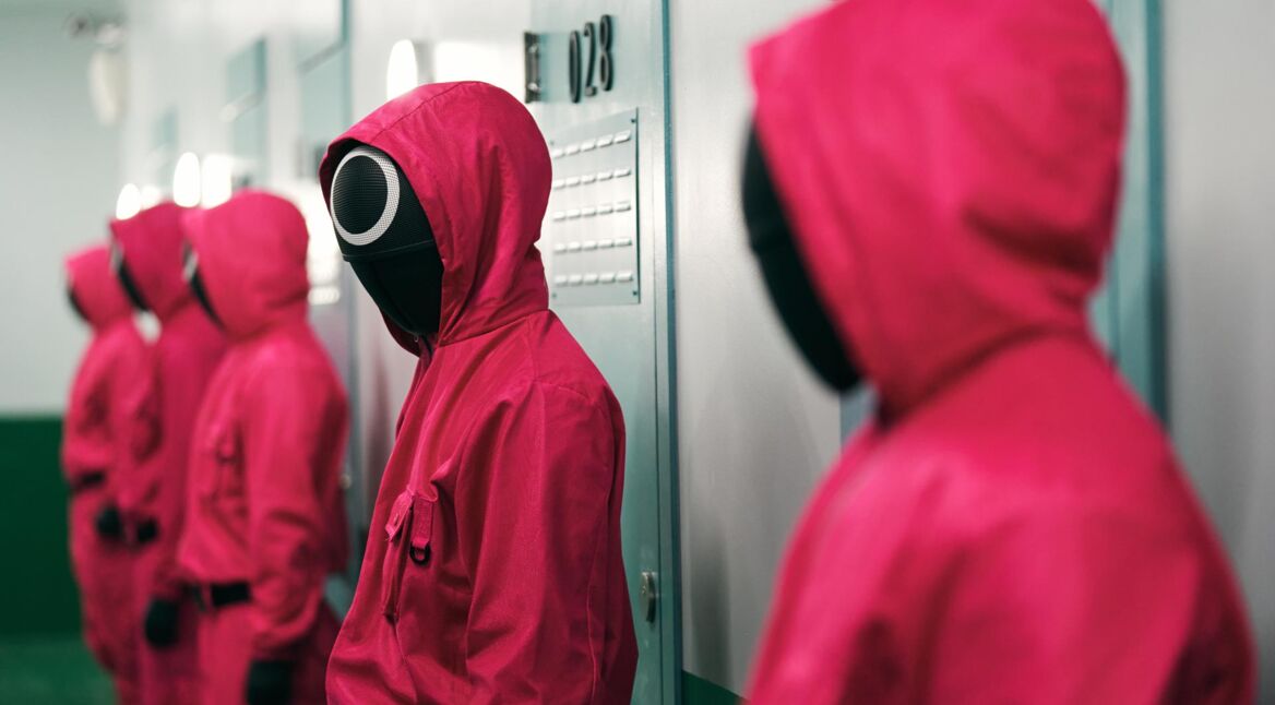 Mehrere Personen in roten Overalls stehen vor einer Wand