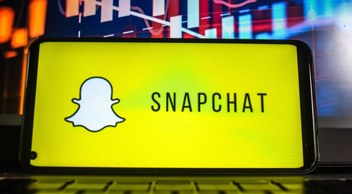 Handy liegt seitlich auf Laptop-Tastatur mit Snapchat-Logo auf dem Display