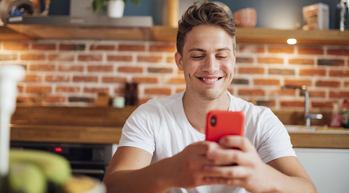 Mann schaut lächelnd auf sein Handy.