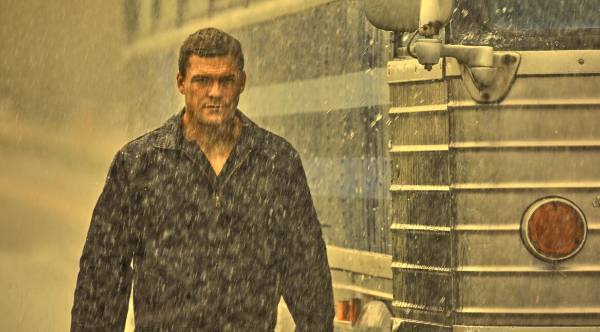 Jack Reacher (Alan Ritchson) steht im Regen neben einem Bus