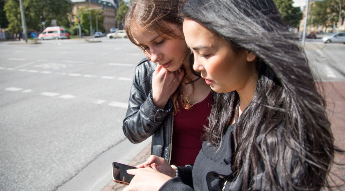 Zwei junge Frauen an Straßenkreuzung schauen auf ein Smartphone