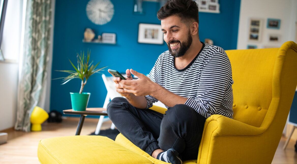 Mann schaut lächelnd auf sein Android-Smartphone.