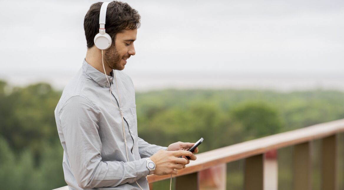 Junger Mann schaut am Strand auf sein iPhone und lächelt.