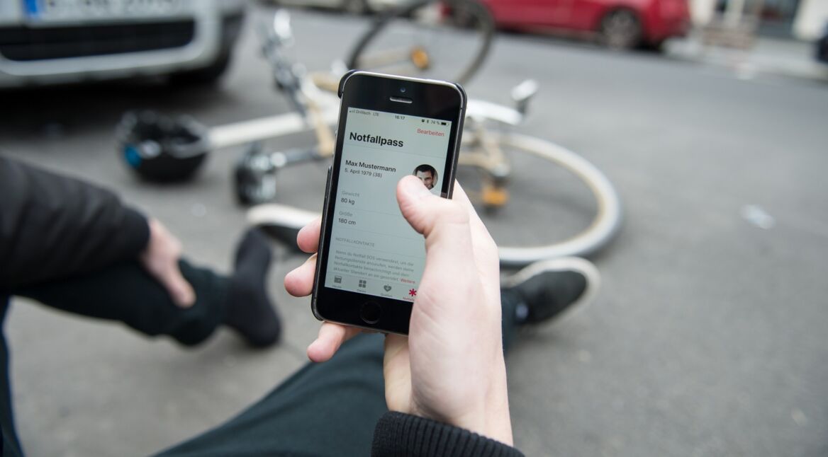 Person sitzt auf der Straße neben Fahrrad und ruft mit iPhone Hilfe