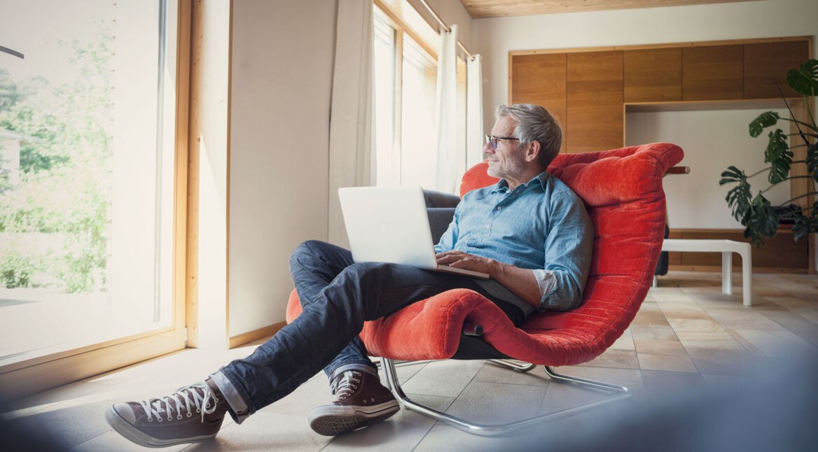 Mann sitzt in einem roten Stuhl mit seinem Laptop
