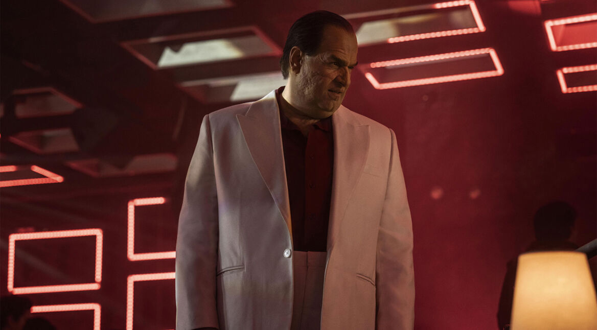 Auf dem Bild zu The Penguin-Serie ist Pinguin zu sehen. Er steht in einem rot gestalteten Raum und trägt ein weißes Sakko.