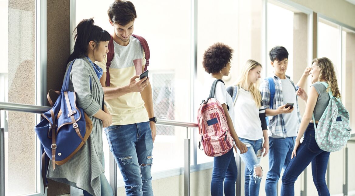 Schüler:innen stehen im Gang und schauen auf Handys