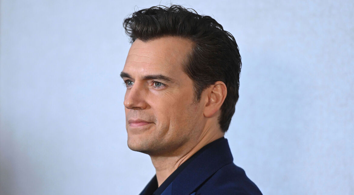 Auf diesem Bild zum Artikel „Voltron-Film mit Henry Cavill“ ist Henry Cavill in einem Profilporträt zu sehen. Er trägt ein dunkelblaues Sakko und blickt leicht lächelnd zur Seite. Sein Haar ist stilvoll nach hinten gekämmt, und der Hintergrund ist dezent und einfarbig, was den Fokus auf sein Gesicht lenkt. Cavill wirkt entspannt und selbstbewusst, passend zu seiner prominenten Rolle im Film.