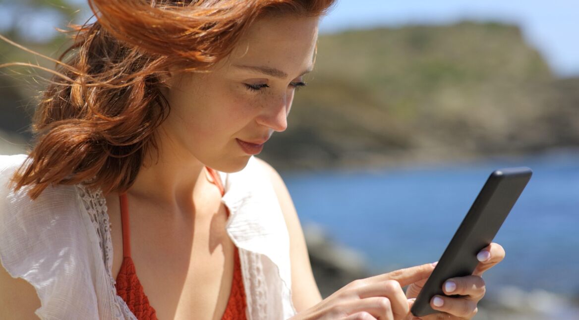 Rothaarige Frau am Meer guckt auf ihr Smartphone