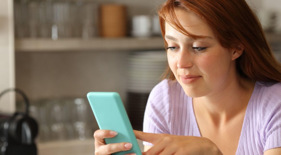 Rothaarige Frau in Küche spielt mit Smartphone