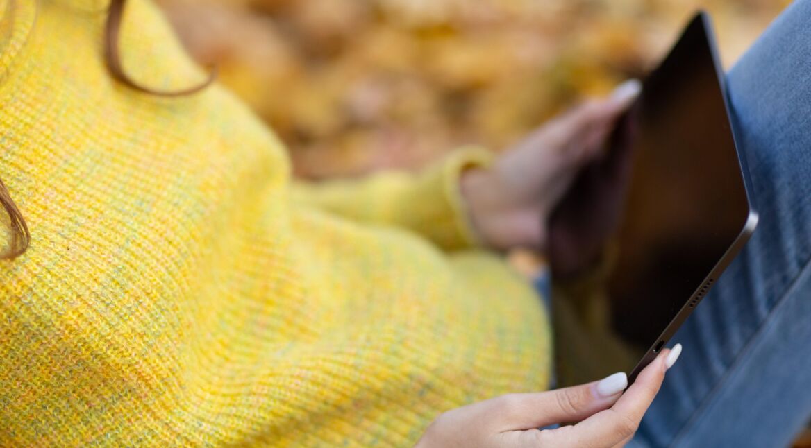 Frau mit gelbem Pullover hält iPad Pro 2021 im herbstlichen Park