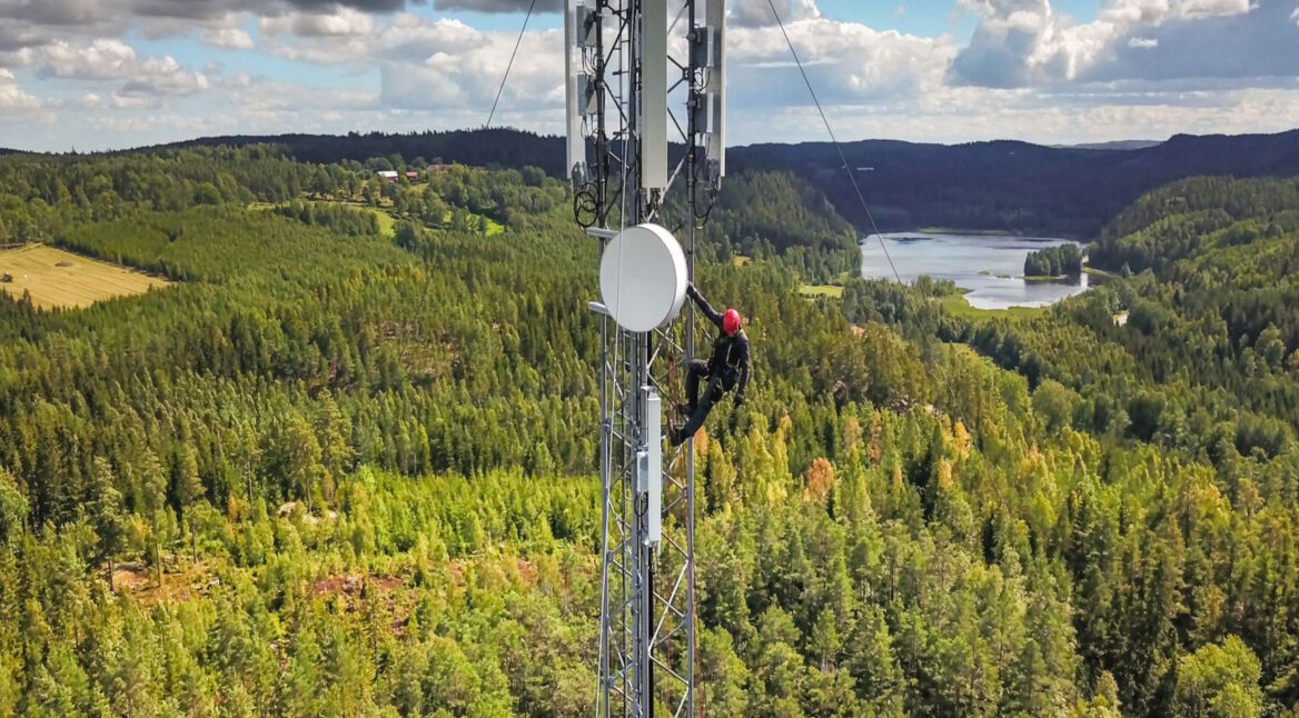 Ein Mensch klettern auf einem Sendemast innmitten eines Waldes.