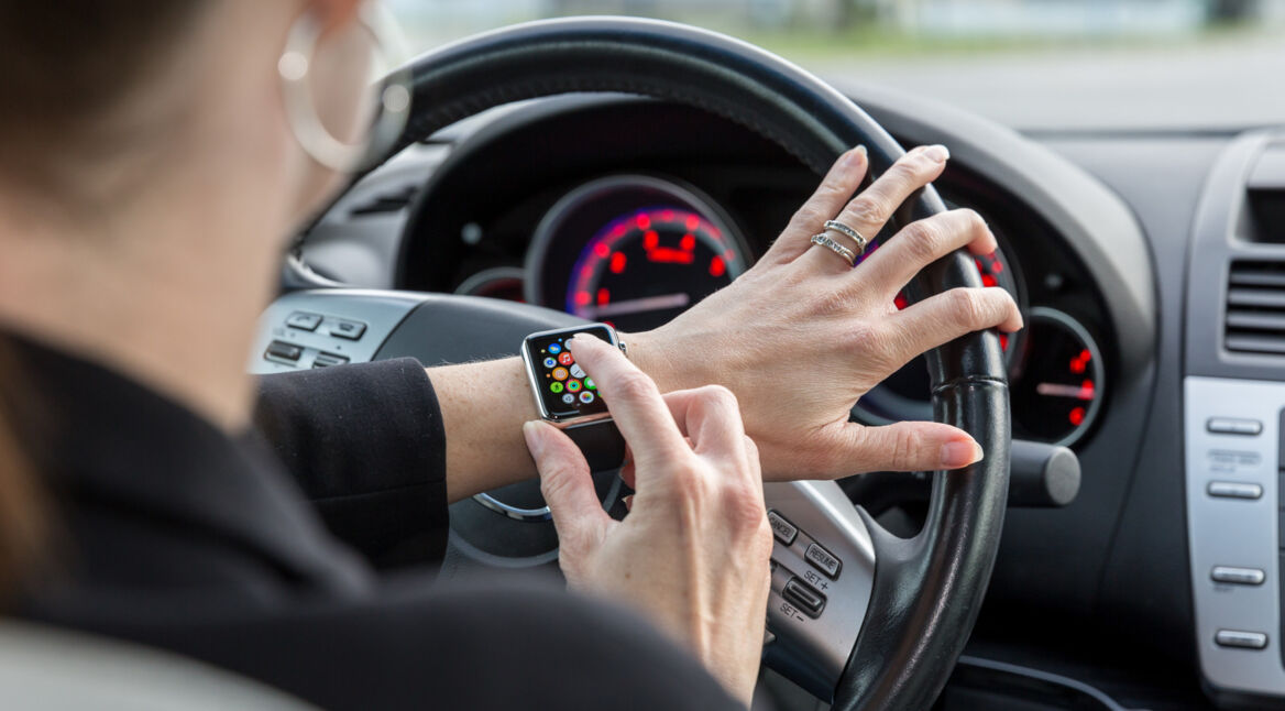 Frau bedient ihre Apple Watch im Auto mit Hand am Steuer