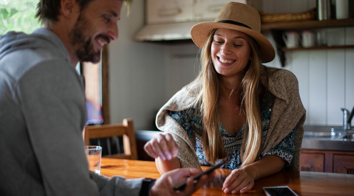 Lächelndes Paar sitzt am Küchentisch und schaut auf ein iPhone